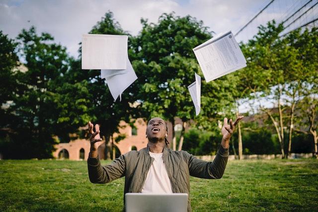 Happy young black male throwing papers while celebrating successful GCSE results