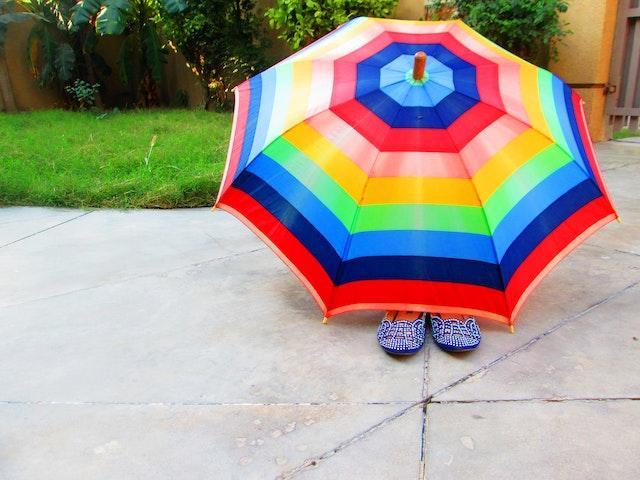Feet of a young person poking out beneath a brightly coloured, striped umbrella. Safeguarding