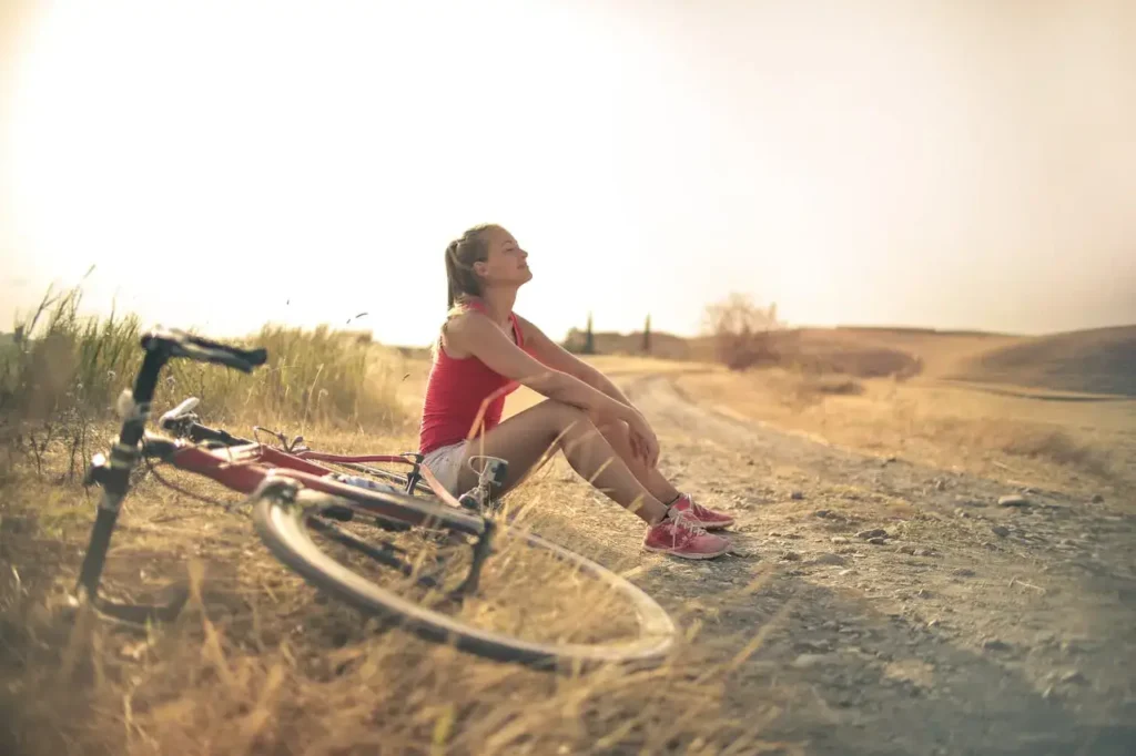 Photo of a woman sat having a mindful moment next to her bike. Mental health benefits of sports